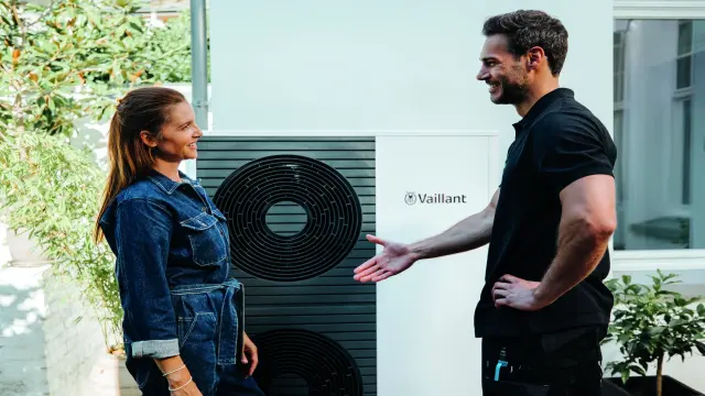 Servisný technik podáva ruku zákazníčke, v pozadí je tepelné čerpadlo Vaillant