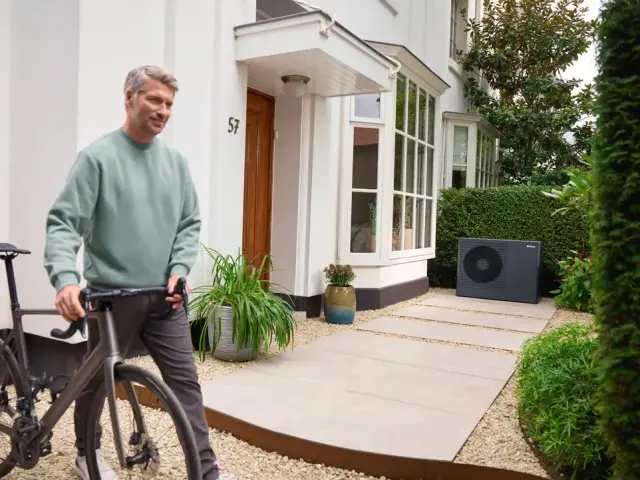 muž kráča s bicyklom a aroTHERM pro stojí pri dome